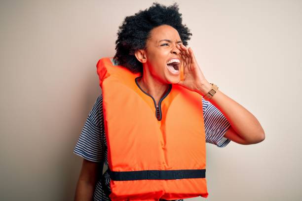 junge afroamerikanische afro-frau mit lockigen haaren trägt orange schutz rettungsweste schreien und schreien laut zu seite mit der hand auf mund. kommunikationskonzept. - life jacket audio stock-fotos und bilder