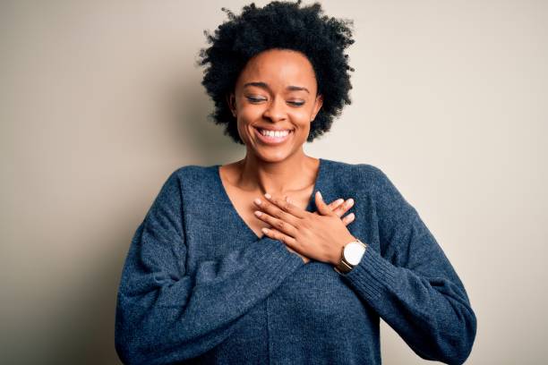 junge schöne afroamerikanische afro-frau mit lockigen haaren trägt lässigen pullover lächelnd mit händen auf der brust mit geschlossenen augen und dankbare geste im gesicht. gesundheitskonzept. - danke stock-fotos und bilder