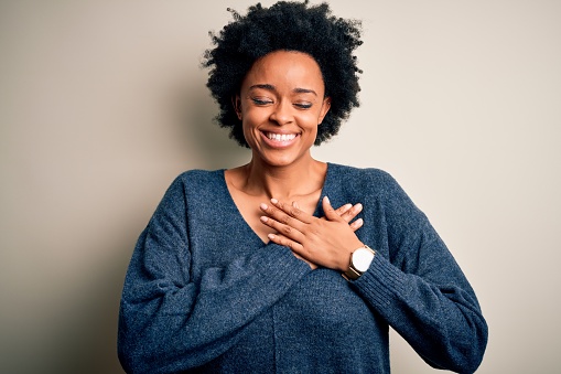 Joven hermosa mujer afro americana con el pelo rizado usando suéter casual sonriendo con las manos en el pecho con los ojos cerrados y gesto agradecido en la cara. Concepto de salud. photo