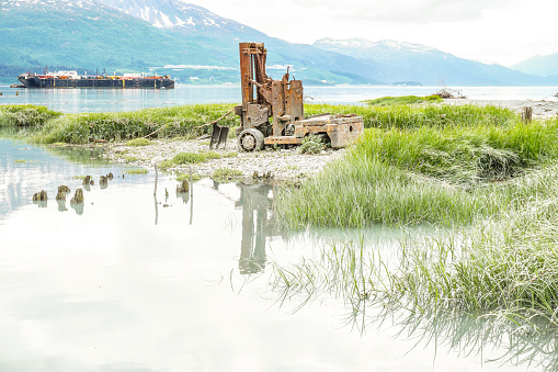 An antique forklift sits abandoned on the shores of Prince William Sound harbor.  The fork lift is a reminder of days gone by. Now it has become a part of the scenic beauty that can be found at the location of Valdez, before the Great Earthquake.