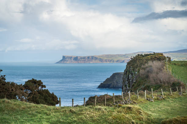 Scenic view of the North Antrim coast, Northern Ireland with distant cliffs and hazy sunshine and clouds in the sky, and wooden fence