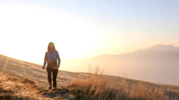 istock Young woman walks through grassy meadow at sunrise 1212282489