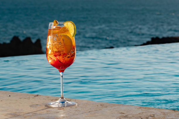istock A cold refreshing red and orange bright colored cocktail with ice cubes and orange slices on pool and ocean background 1212286076