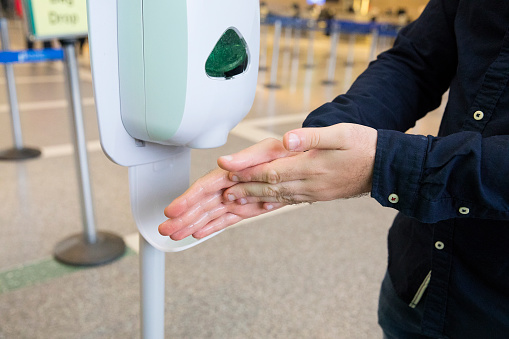 Man at the airport washes his hands using hand sanitizer dispenser in the airport to combat flu, cold and coronavirus.