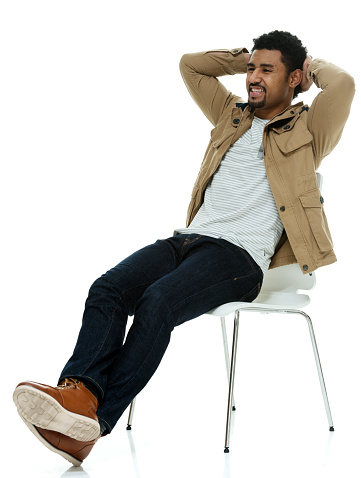 Side view of aged 20-29 years old with black hair pacific islander ethnicity male relaxing in front of white background wearing pants who is cheerful with hands behind head