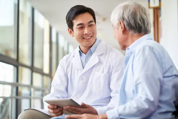 Photo of young asian doctor talking to senior patient in hospital