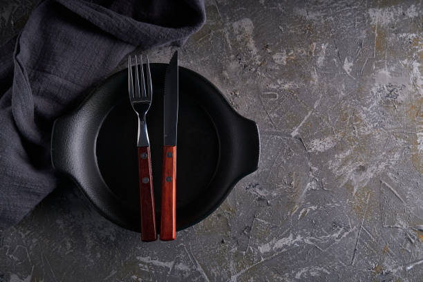 灰色の背景vertcalコピースペースにフォークとナイフを持つ黒い料理 - vertcal ストックフォトと画像