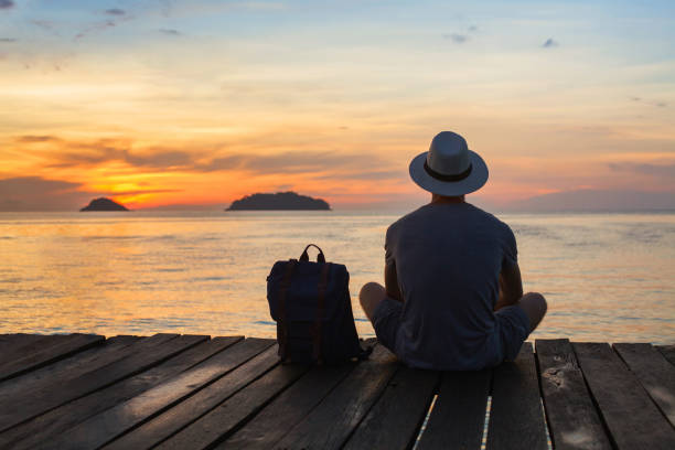 放浪者旅行、海の近くに座っているバックパックを持つ観光客 - mind trip ストックフォトと画像