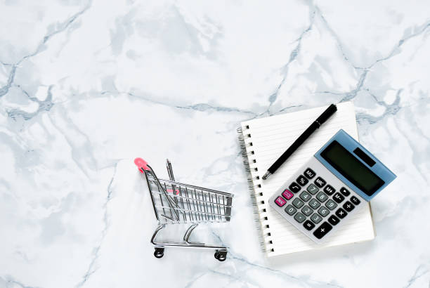 istock Top view objects , calculator, black pen on  notebook  with small mini shopping cart on  white gray brick background. Idea business and finance concept. sensitive 1212308854