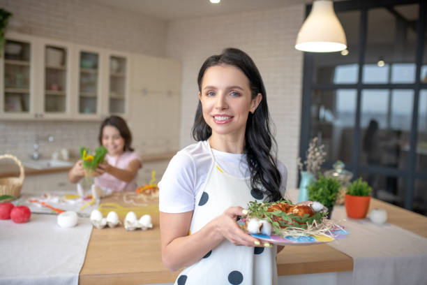 istock Cute smiling woman holding in hands a tray with easter buns and looking contented 1212309639