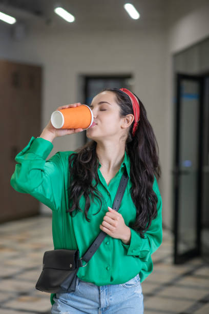istock Young woman walking down the hall drinking coffee. 1212309882
