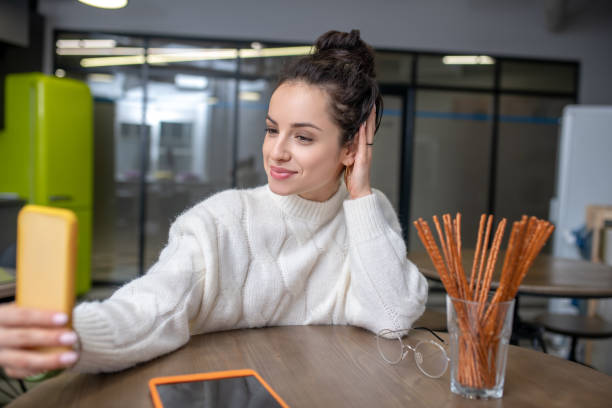 istock Young woman sitting at the table, making selfie 1212309993