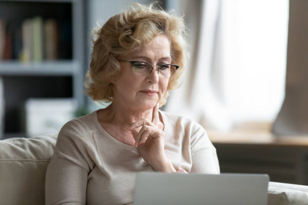 istock Pensive senior woman using laptop gadget at home 1212315787
