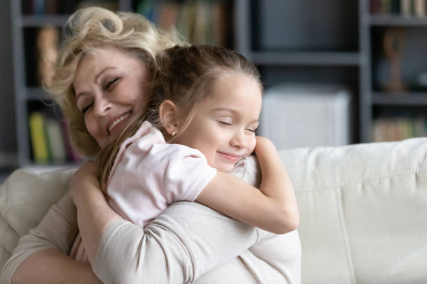 Happy senior granny cuddle with cute preschooler granddaughter Happy senior grandmother sit on couch in living room hugging cute little preschooler granddaughter, smiling mature 70s granny embrace cuddle with small grandchild, show love and care, bonding concept grandmother stock pictures, royalty-free photos & images