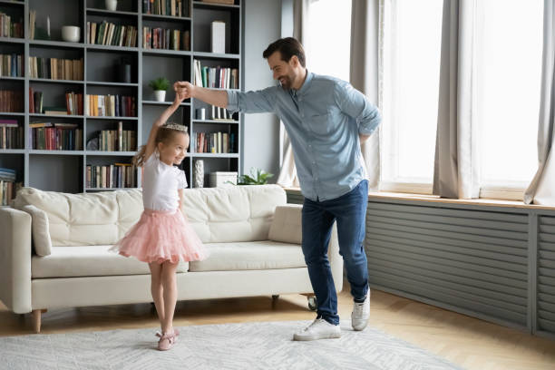 Happy father have fun play with little daughter Happy young father dance with cute little daughter princess wearing crown and beautiful skirt, smiling dad have fun engaged in funny activity playing with small preschooler girl child at home dancing dad stock pictures, royalty-free photos & images
