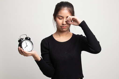 Sleepy young Asian woman with a clock in the morning on white background
