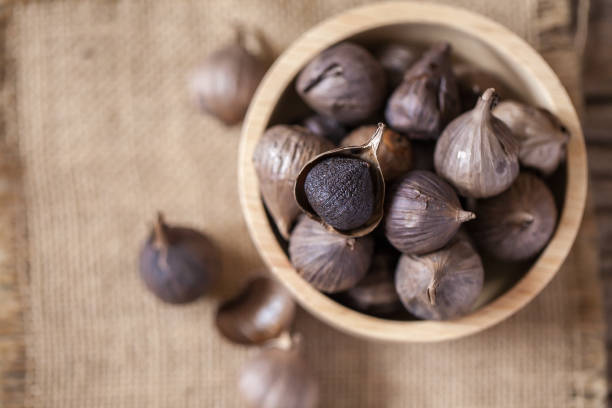 Black garlic on sack cloth and wooden table Black garlic on sack cloth and wooden table garlic bulb photos stock pictures, royalty-free photos & images