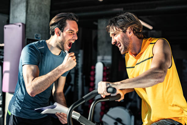 happy coach cheering for athletic man on stationary bike in a gym. - spinning instructor exercising gym imagens e fotografias de stock