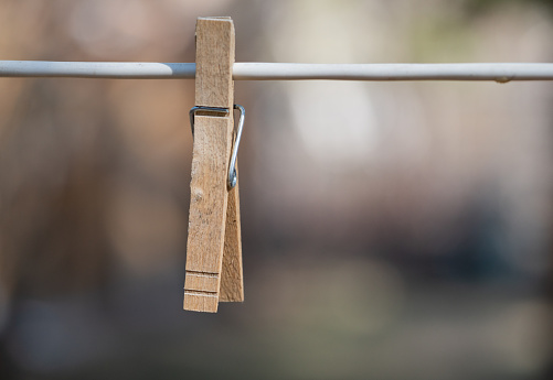 Single wooden clothespin hanging from a cable in a backyard.  Background is blurred with sharp focus on the clothespin.
