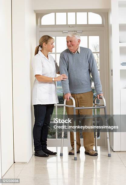 Foto de Cuidador Ajudando Sênior Homem Idoso Usando Uma Caminhada De Quadro e mais fotos de stock de 60 Anos