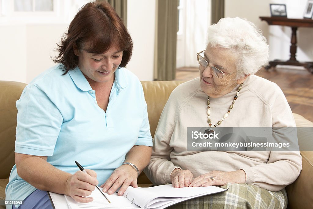 Sênior mulher na discussão com a saúde visitante em casa - Foto de stock de 70 anos royalty-free