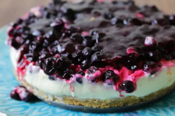 Stock photo showing blackcurrant cheesecake with buttery biscuit base, vanilla mascarpone cream cheese for dessert pudding after restaurant dinner.