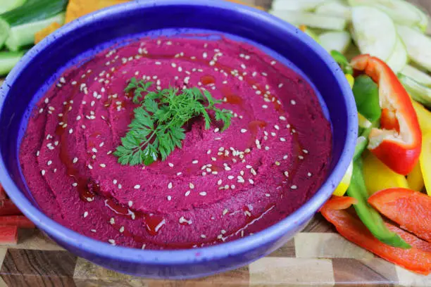 Stock photo of beetroot hummus platter, healthy eating vegan appetiser, Greek cuisine food (hommus / houmous) made from chickpeas, olive oil, tahini paste, roasted beetroot and garlic, in purple colours and flavours, served with Julienne carrot, cucumber, gravy smith apple, nachos, peppers