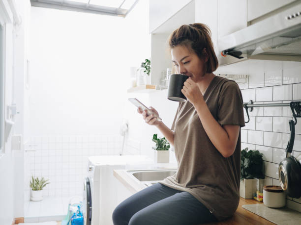 istock Young woman sitting in cozy kitchen and working on her mobile. 1212332494