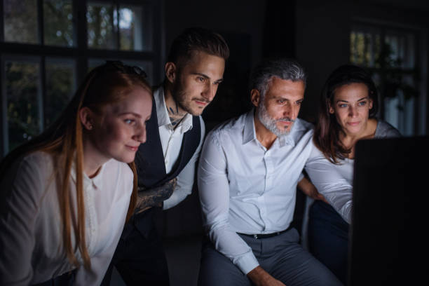 istock Group of businesspeople with computer indoors in office, working late. 1212337195