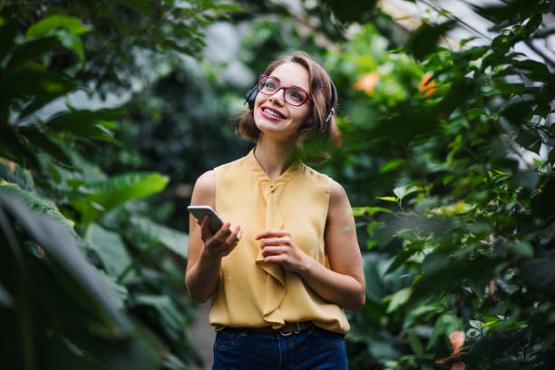 istock Young woman with smartpone standing in botanical garden. Copy space. 1212337723
