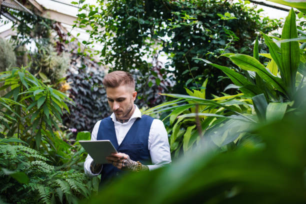 istock Young man with tablet standing in botanical garden, working. 1212338276