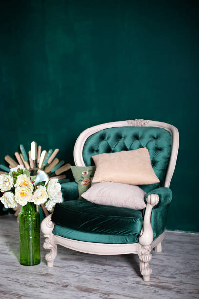 エメラルドの壁の近くに花瓶と花束を持つアンティークベルベットグリーンのアームチェア。緑の背景に隔離されたアームチェア。リビングルームのヴィンテージチェア。家具の家。 クラシ - vehicle interior green sofa indoors ストックフォトと画像