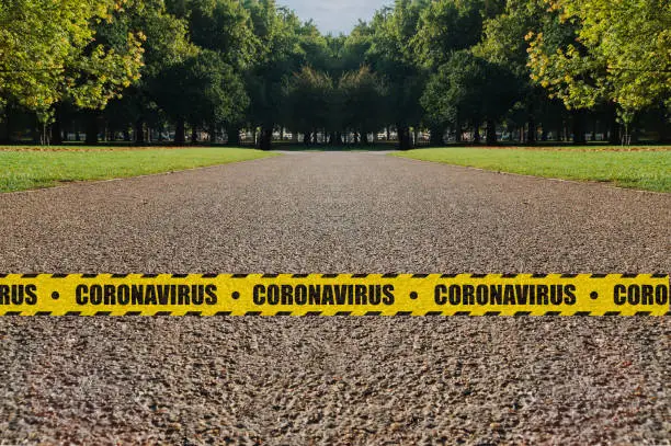 Parks lockdown concept: an empty park bordered by a yellow and black safety tape with the word coronavirus after closing to prevent contagion spread.