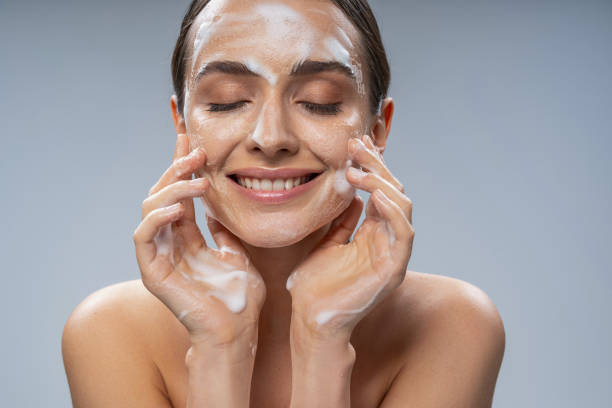 Young pretty lady washing her face with soap Portrait of smiling attractive woman touching face by hands while cleansing the skin from makeup. Isolated on grey background. Cosmetics and care concept soap sud photos stock pictures, royalty-free photos & images