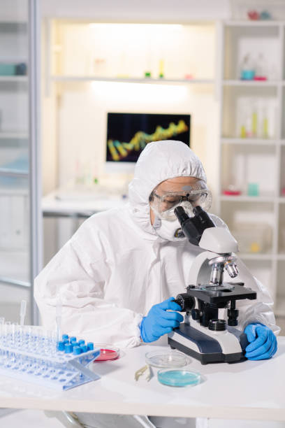 istock Scientist or chemist in protective workwear sitting at workplace by microscope 1212345449