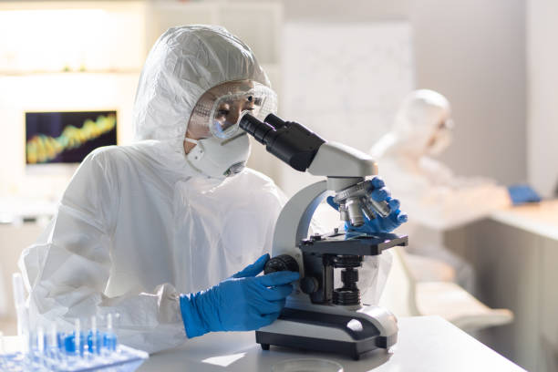 funcionária de laboratório ou pesquisadora olhando para novo elemento químico no microscópio - genetic research men chemical protective glove - fotografias e filmes do acervo