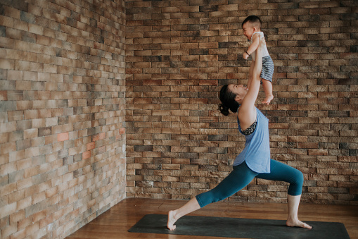 an asian chinese female yoga instructor workout together with her 9 month old baby boy son in the living room with brick wall on yoga met
