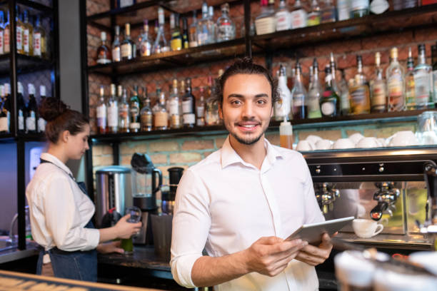 istock Young cheerful waiter with touchpad standing in front of camera 1212350526