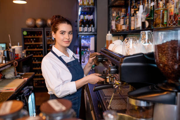 istock Young waitress of cafe looking at you while standing by coffee machine 1212350569