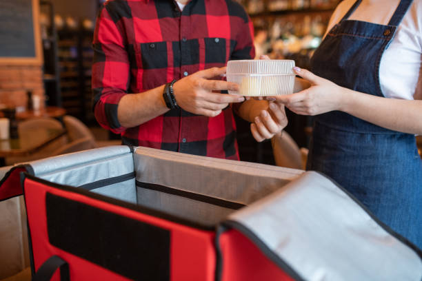 istock Waiter of cafe passing plastic container with order of client to courier 1212350593