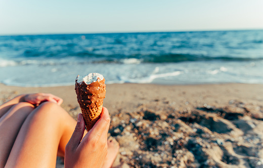Woman holding chocolate ice cream in waffle cone on the beach