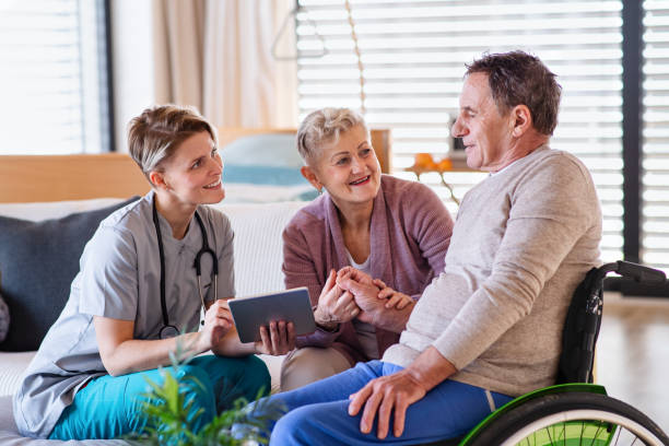 A healthcare worker visiting senior patient in wheelchair at home. A healthcare worker with tablet visiting senior patient in wheelchair at home, talking. paraplegic stock pictures, royalty-free photos & images