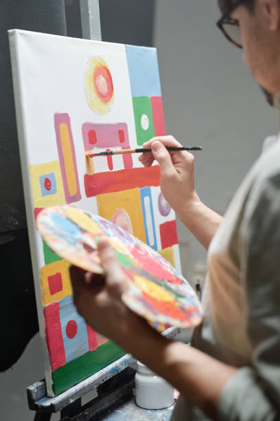istock Hand of young artist holding color palette while using paintbrush during work 1212356918
