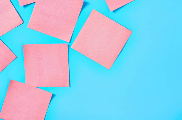 istock Scattered many pink square blank paper stickers on blue background. Copy space. Top view 1212357801