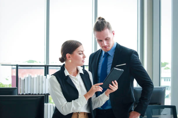 istock Young smart businessman and businesswoman using digital tablet together, discussion about work in the office 1212360207
