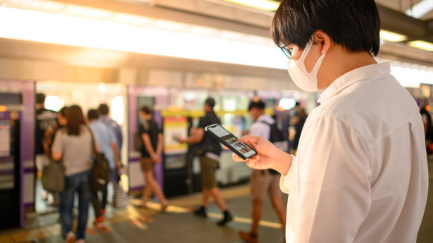 mężczyzna w masce za pomocą telefonu na stacji skytrain - bangkok mass transit system zdjęcia i obrazy z banku zdjęć