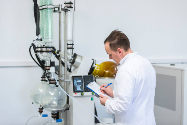 Scientist controlling rotavapor machine during CBD and CBDa oil extraction Scientist holding paper board and controlling rotational vaporizer during CBD oil extraction. Machine has green condenser and rotational flask where CBD hemp oil extraction is in process. tincture photos stock pictures, royalty-free photos & images