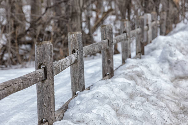 An old wooden fence that is held together with willow rods and separates two snowy pastures from each other. In addition, the fence is reinforced with a barbed wire.
