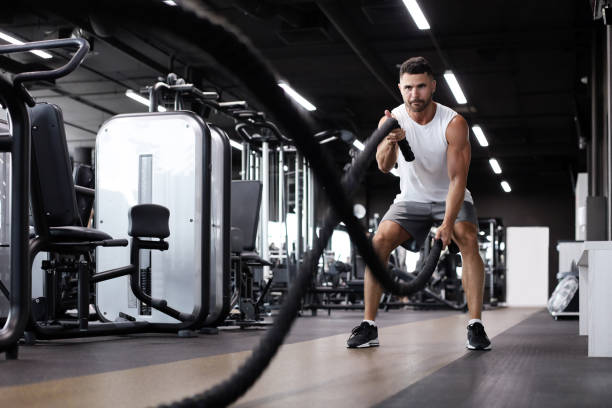 istock Athletic young man with battle rope doing exercise in functional training fitness gym. 1212373738