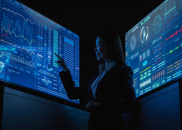 istock The business lady standing between blue monitors in the dark office 1212375020